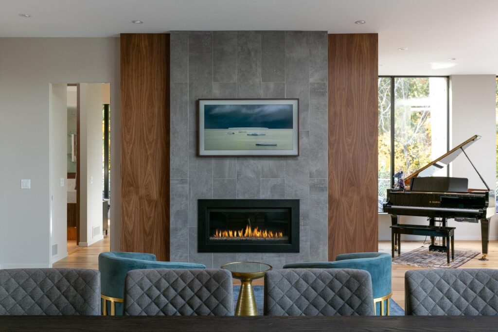 Living room with grey stone fireplace, walnut accent panels, teal chairs and grand piano
