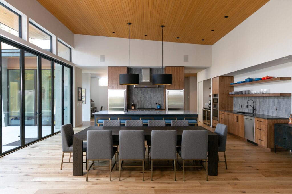 Open concept dining and kitchen with vaulted cedar ceiling, blue island and grey upholstered chairs