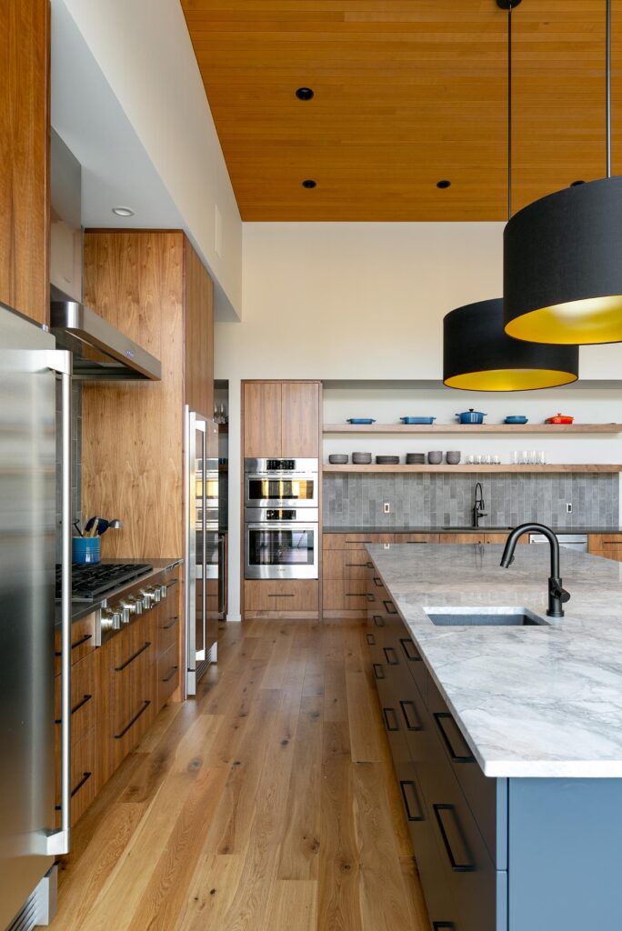 Gourmet kitchen with walnut cabinetry, marble island, cedar ceiling and black drum pendants