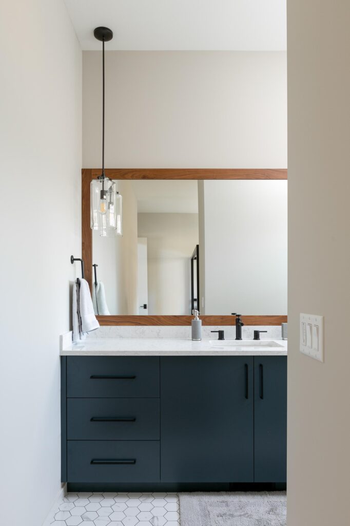 Guest bathroom vanity with dark teal cabinetry, walnut-framed mirror and hex tile floor