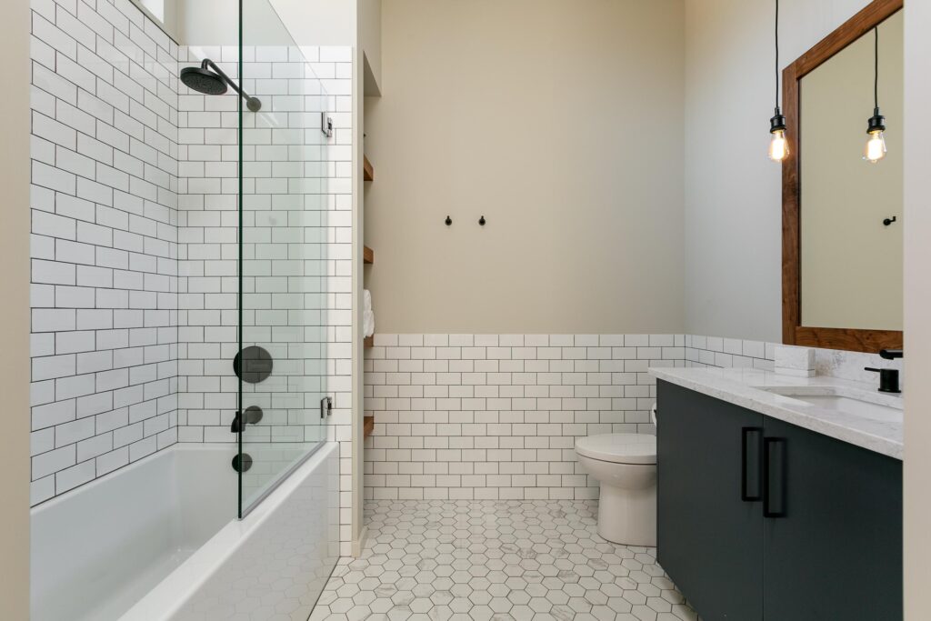 Guest bathroom with white subway tile, glass-enclosed tub, teal vanity and Edison pendants