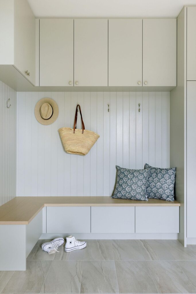 Custom mudroom with sage cabinetry, shiplap bench and brass hooks