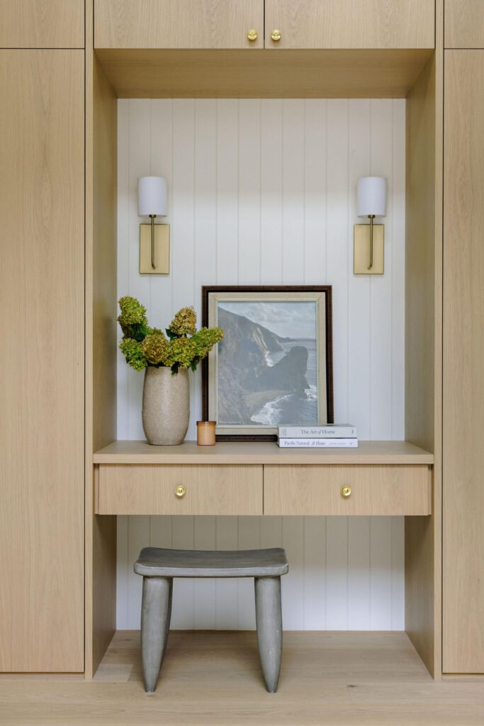 Oak vanity nook detail with brass sconces, coastal art and dried hydrangeas