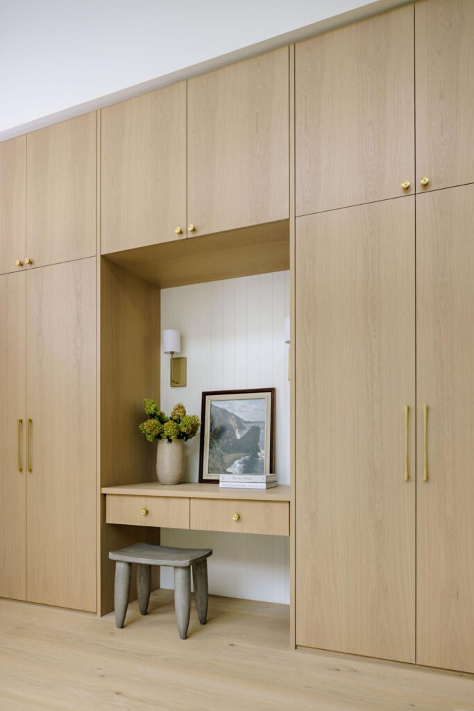 Floor-to-ceiling oak wardrobe wall with built-in vanity nook and brass hardware