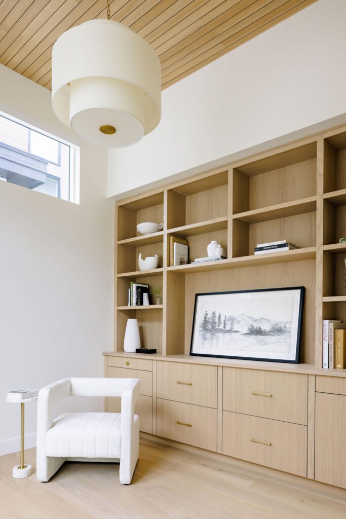 Built-in oak media wall with open shelving, brass pulls and vaulted cedar ceiling