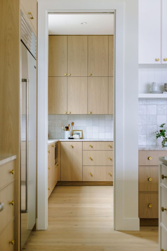 View through kitchen doorway into butler's pantry with oak cabinetry and brass hardware