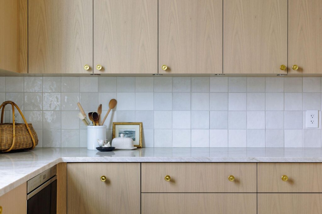 Oak cabinetry detail with zellige tile backsplash, marble counter and brass knobs