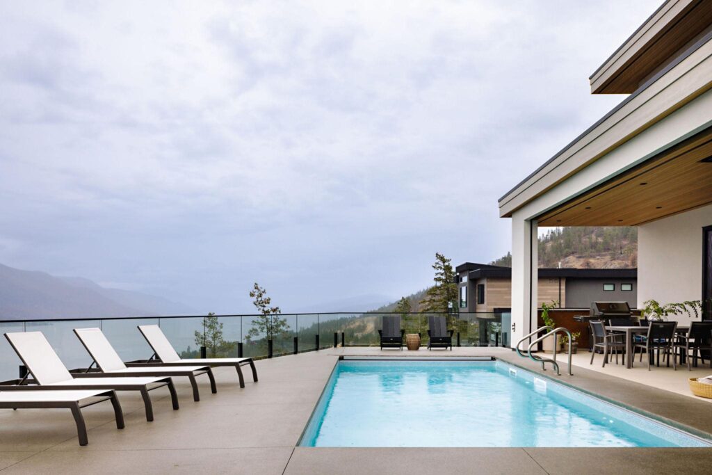 Hillside pool terrace with chaise lounges, glass railing and Okanagan Lake panorama