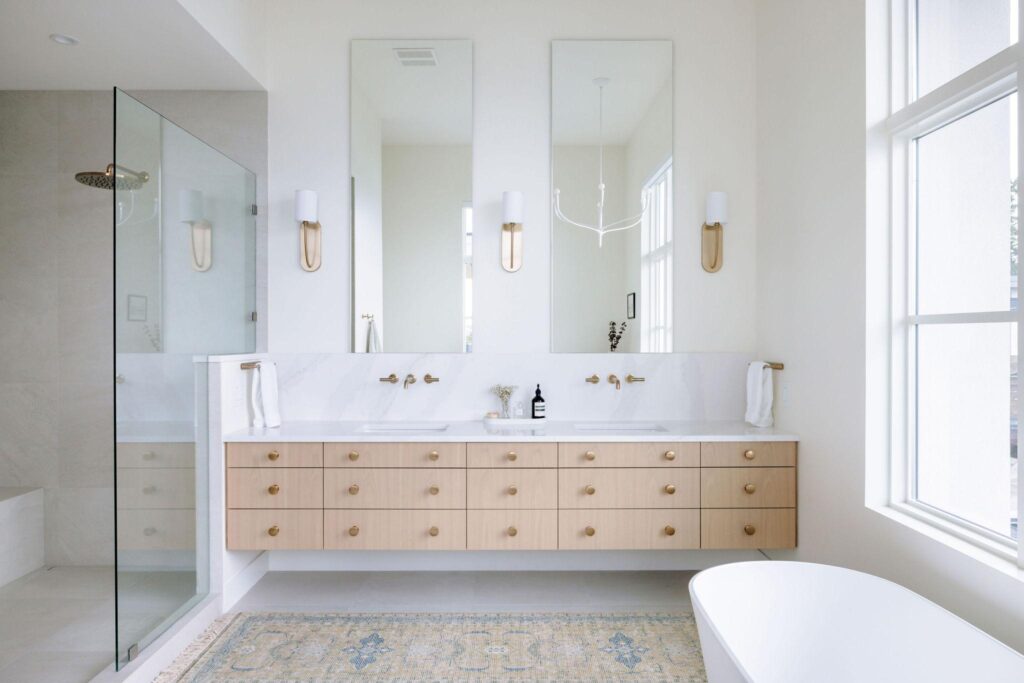 Floating oak double vanity with marble top, brass fixtures and glass shower in primary ensuite