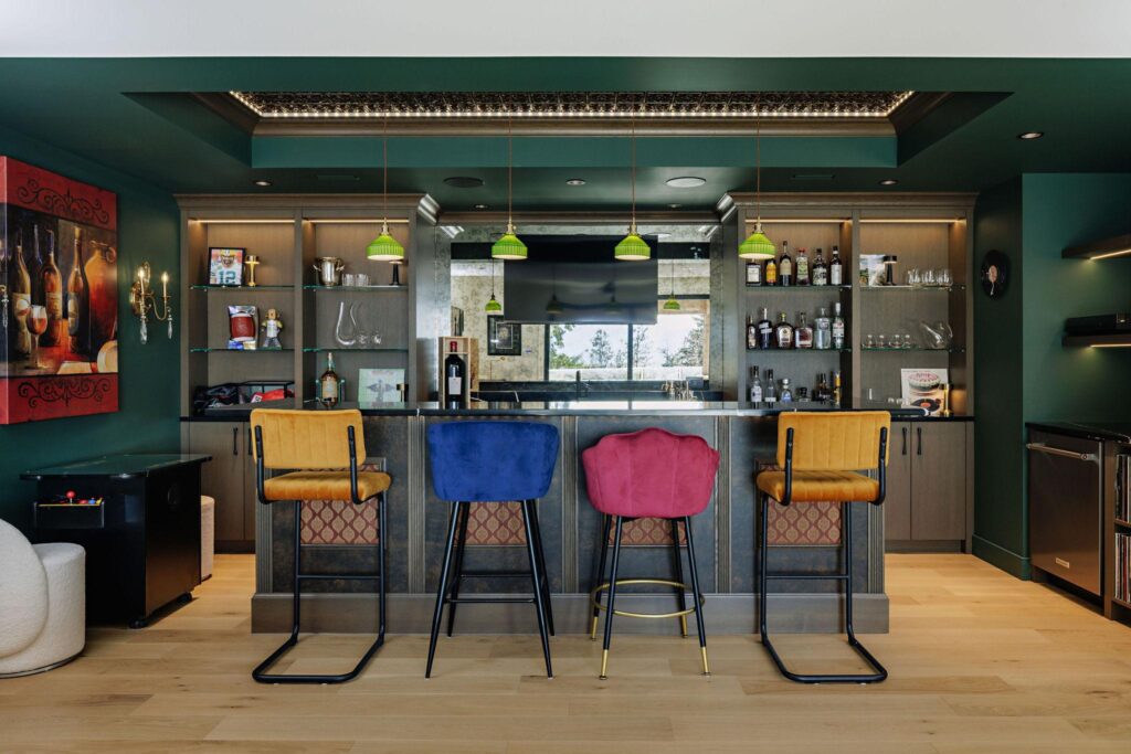 Custom home bar with deep green walls, colorful velvet stools and built-in shelving