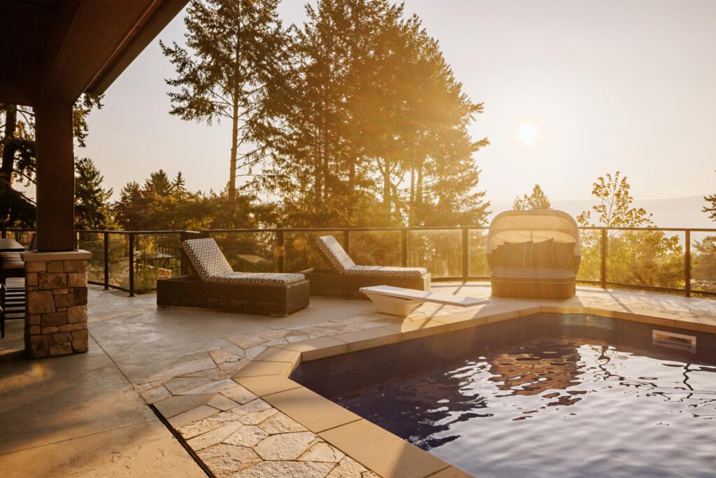 Luxury pool deck with lounge seating, glass railing and Okanagan sunset views