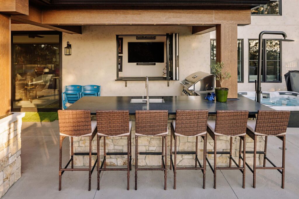 Outdoor bar with stone base, black granite countertop, wicker stools and built-in TV
