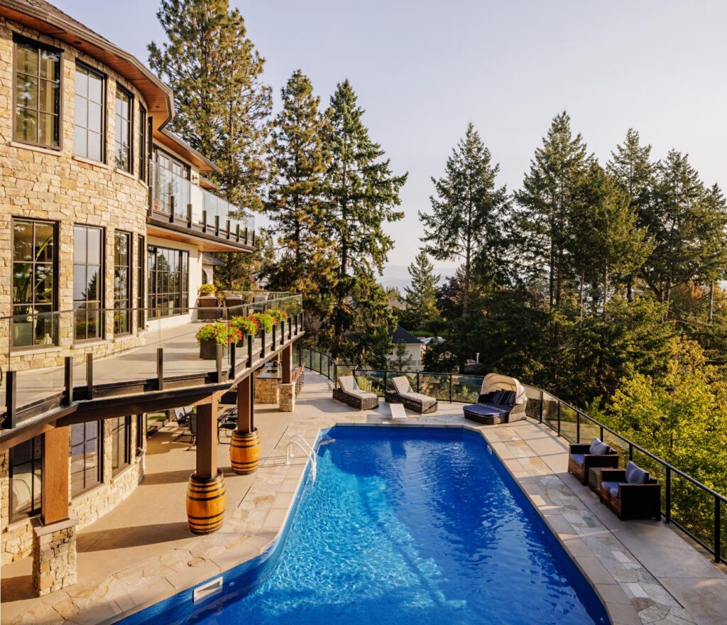 Stone and stucco hillside home with lap pool, multiple decks and Okanagan views