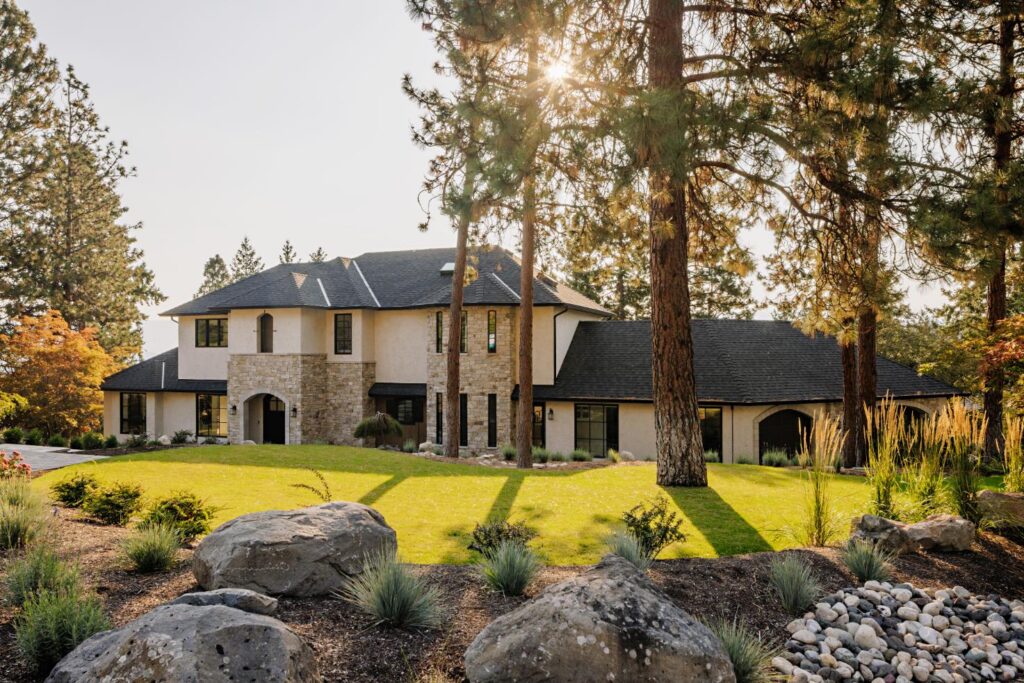 Tuscan-inspired luxury home with stone and stucco exterior surrounded by Okanagan pines at sunset